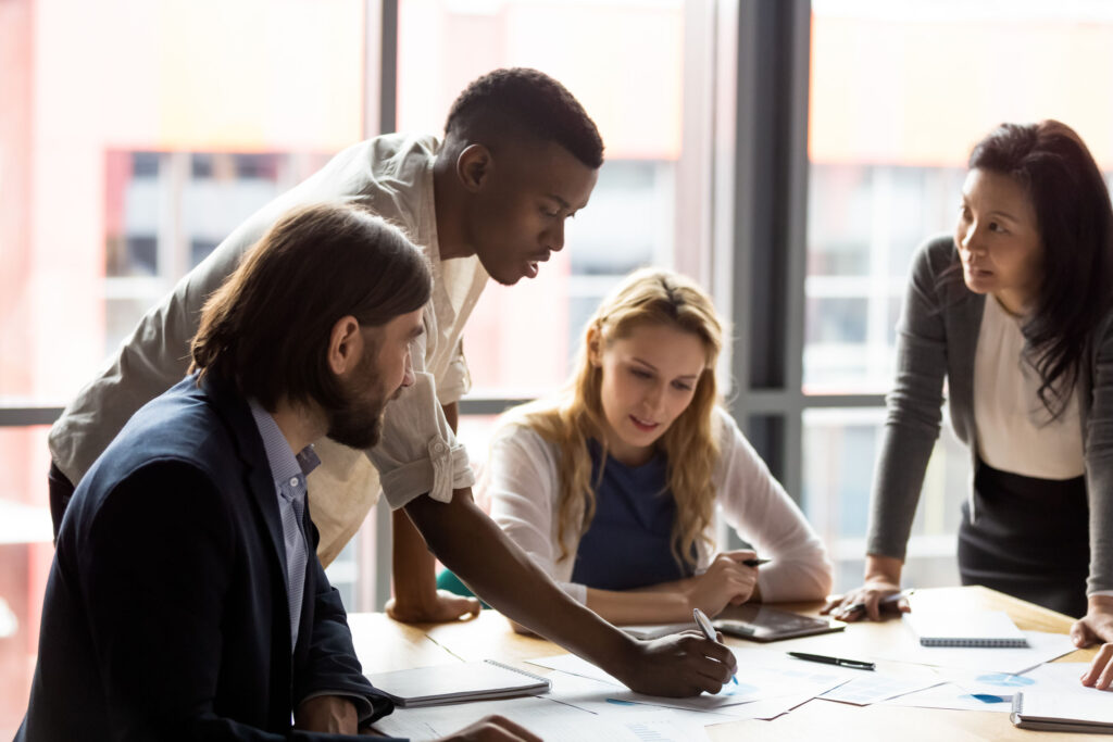 A leader leans in at the table with their team, modeling how to ask better questions to build trust, spark collaboration, and improve communication.