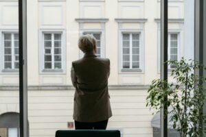 Leader standing alone looking out office window illustrating depleted energy and disengagement under stress